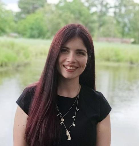 Olga Karadimou is standing in front of a pond with long dark brown hair with red streaks